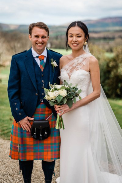 Groom and bride stand on stones pathway in front of grass scenery