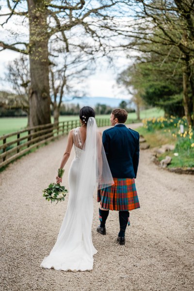 Bride and groom walk along pathway farm setting