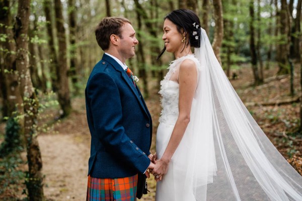 Bride and groom face each other hand in hand in forest setting