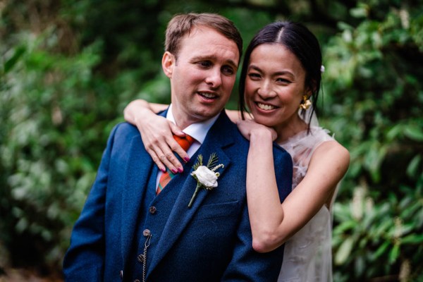 Bride smiles laughs while hugging groom from behind