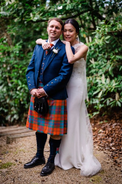 Bride hugs groom from behind in forest setting