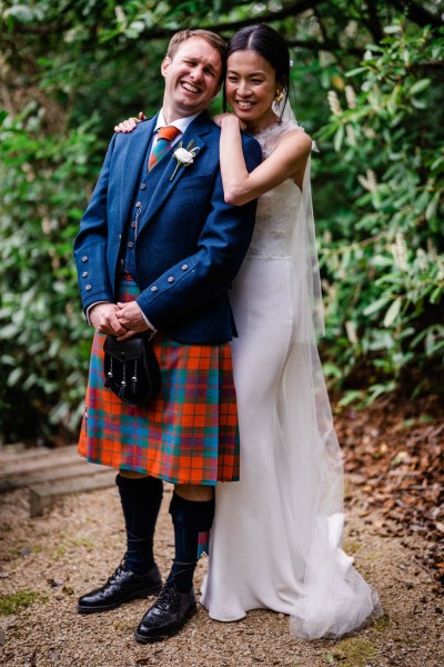 Bride hugs groom from behind in forest setting