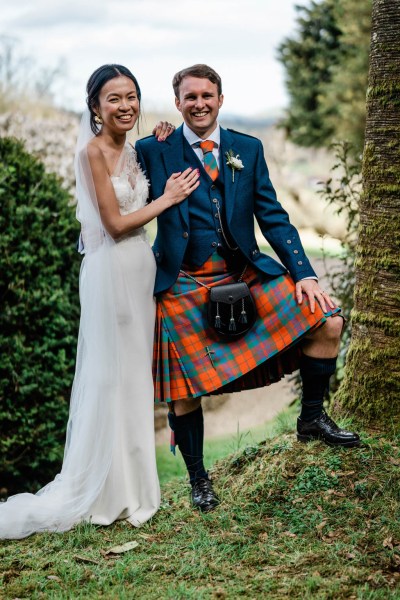 Groom has his leg on tree ground bride smiles