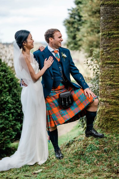 Groom has his leg on tree ground bride smiles