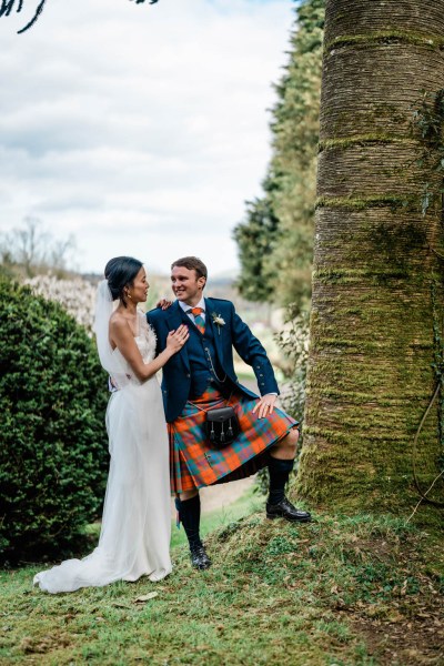 Groom has his leg on tree ground bride smiles