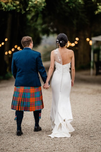 Couple bride and groom walk hand in hand from behind on pathway