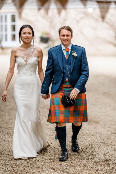 Bride and groom outside wedding venue holding hands walking along pathway