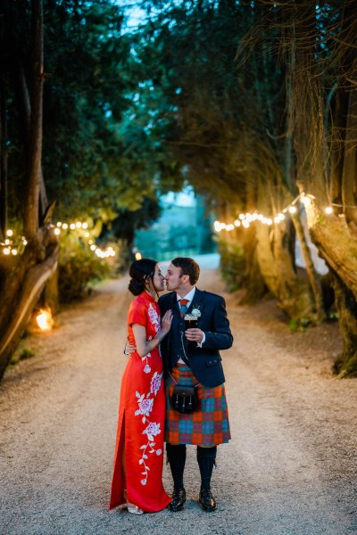 Bride and groom kiss on pathway lights in background