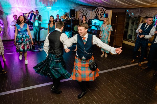 Groom dancing with man friend guest on dancefloor wearing kilts