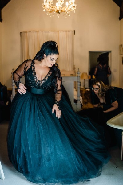 Bride poses in dark blue black bridal gown holding dress looking down