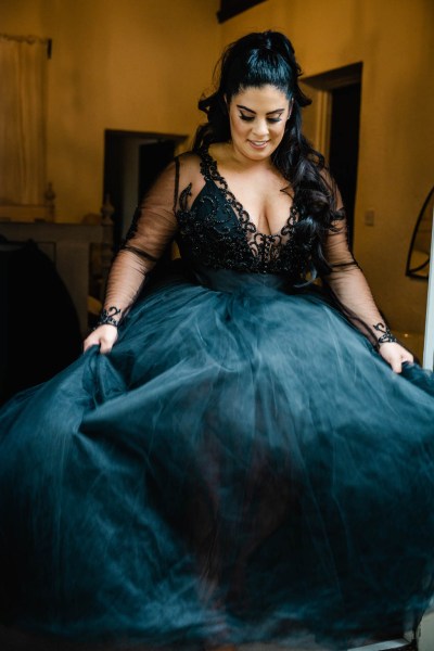 Bride poses in dark blue black bridal gown holding dress