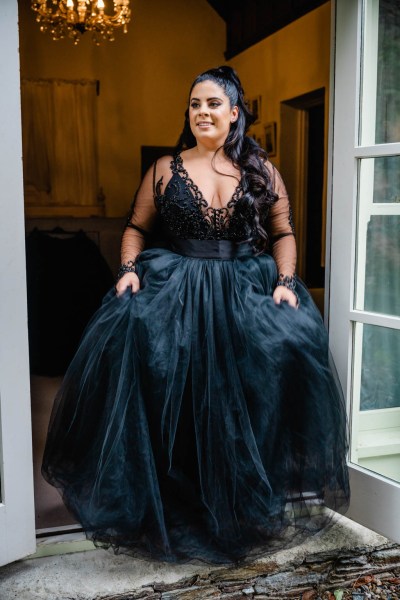 Bride poses in dark blue black bridal gown holding dress