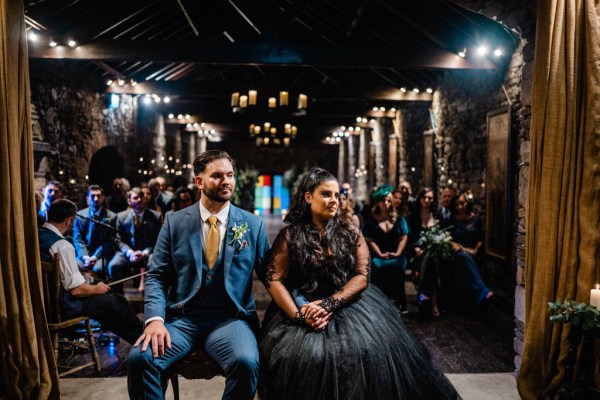 Bride and groom holding hands sitting in front of guests