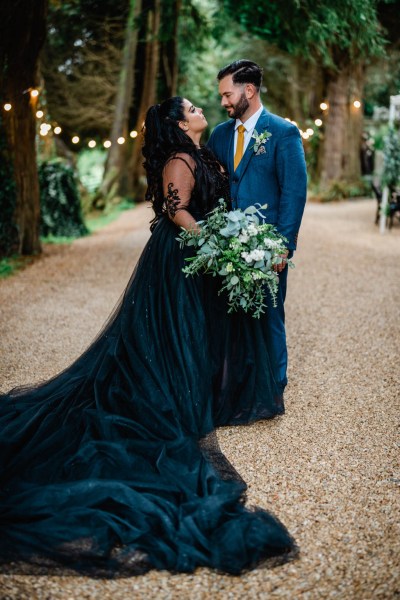 Bride and groom look at each other in park garden pathway lights in background