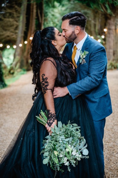 Bride and groom kiss in park garden pathway lights in background