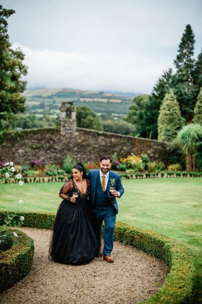 Bride and groom hold beer/Guinness beverages in garden walking