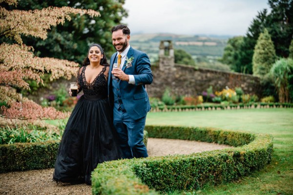 Bride and groom hold beer/Guinness beverages in garden walking