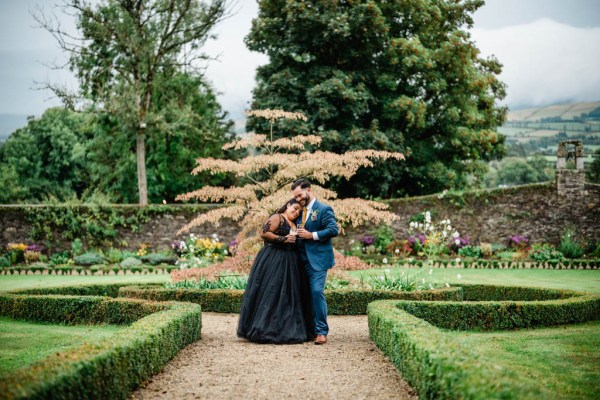 Bride and groom hold beer/Guinness beverages in garden walking head on shoulder hugging