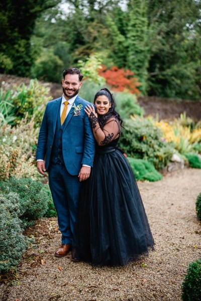 Bride and groom pose for a photo in garden on pathway