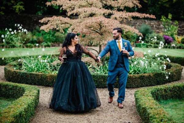 Bride and groom walk hand in hand in the garden