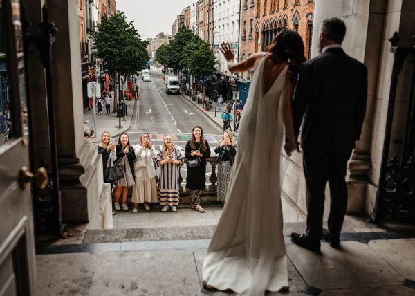 Bride and groom stand at ceremonial entrance guests outside clapping