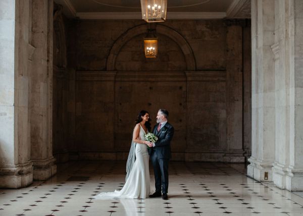 Bride and groom walking on checkered floor tiles together hand in hand holding hands flowers bouquet