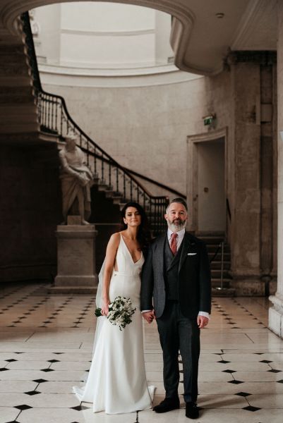 Bride and groom walking on checkered floor tiles together hand in hand holding hands flowers bouquet