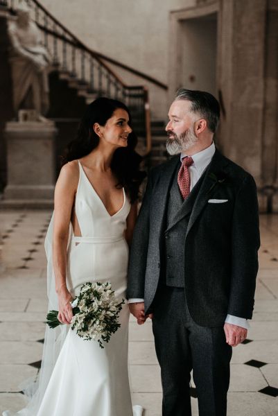 Bride and groom walking on checkered floor tiles together hand in hand holding hands flowers bouquet looking at each other