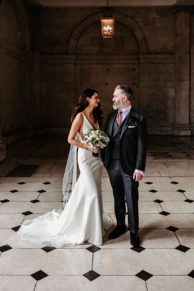 Bride and groom walking on checkered floor tiles together hand in hand holding hands flowers bouquet looking at each other