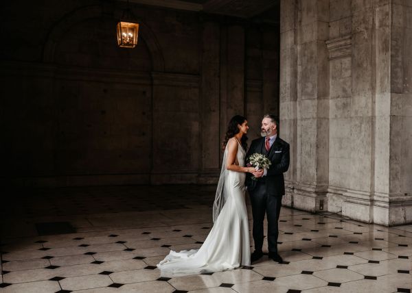 Bride and groom walking on checkered floor tiles together hand in hand holding hands flowers bouquet looking at each other