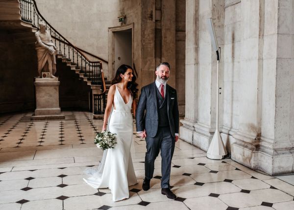 Bride and groom walking on checkered floor tiles together hand in hand holding hands