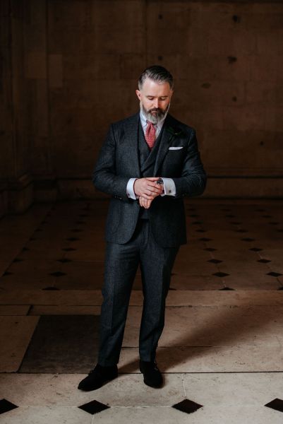 Groom stands on his own checkered floor tiles looking at watch