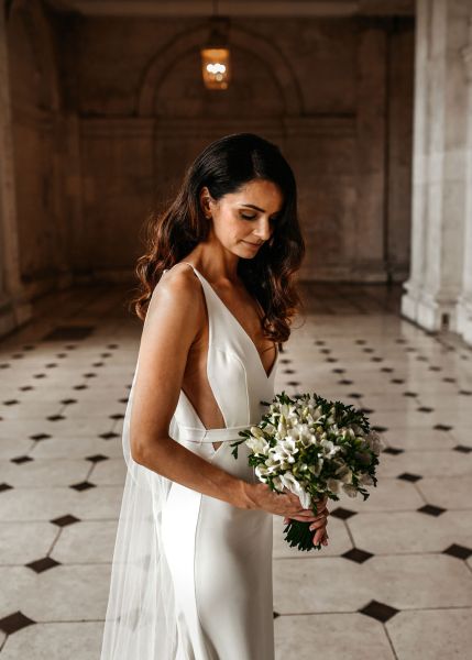 Bride standing on checkered floor tiles looking down at bouquet