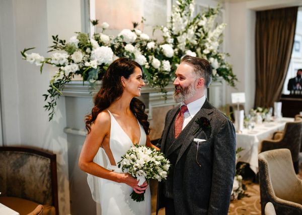 Bride and groom stand holding bouquet look at each other