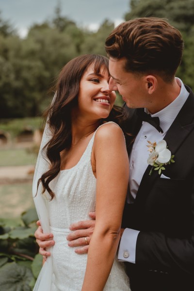 Groom goes in for a kiss with bride hug from behind