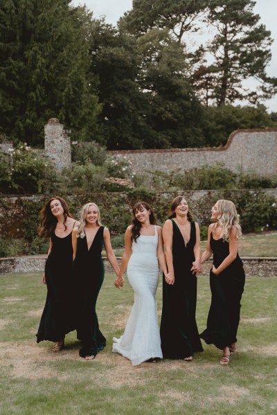 Bride and bridesmaids in black exterior garden shot holding hands