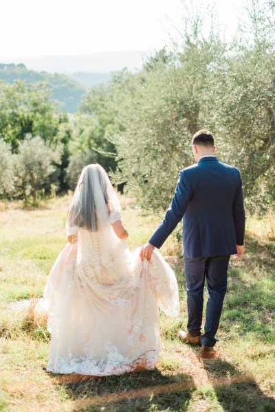 Bride and groom walk from behind long train dress through garden