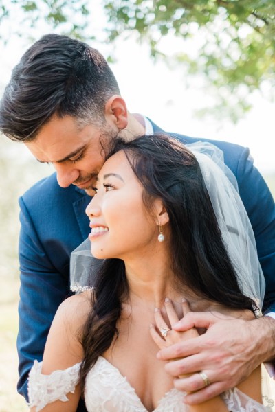 Groom hugs bride from behind in garden close up