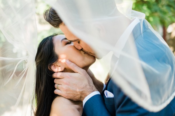 Bride and groom with veil over couple kissing kiss