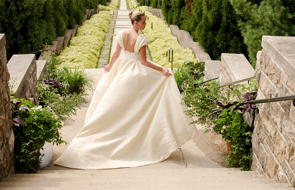 Bride shows off back of dress satin walking down steps in garden