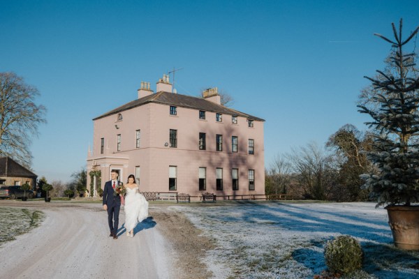 Bride and groom walk along pathway to wedding venue