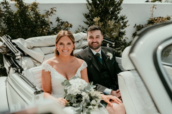 Bride and groom sit in white wedding car together