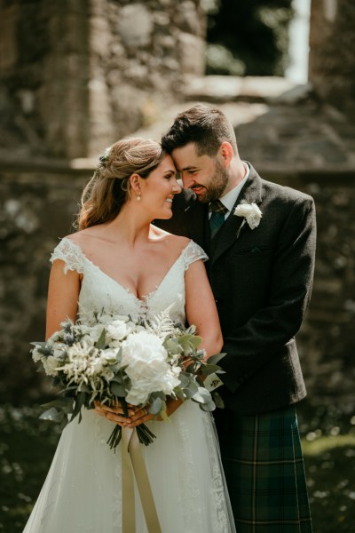 Couple touch foreheads outside of church setting on grass bride holds bouquet