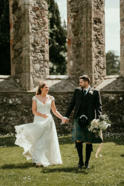 Bride and groom walk in the sunshine hand in hand on the grass