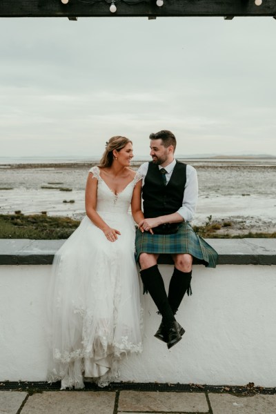 Bride and groom sit in front of beach looking at each other