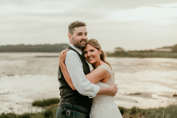 Beach sea ocean in background bride and groom on grass hugging embracing