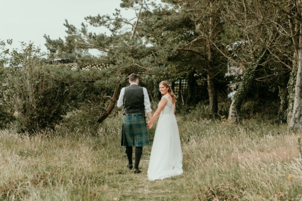 Bride and groom on grass in forest holding hands