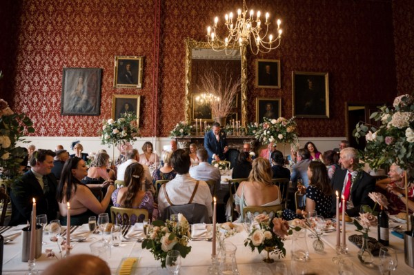 Bride and groom seated at table chandelier overhead with guests