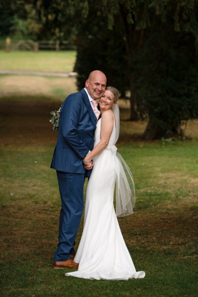 Bride and groom holding each other in forest park setting