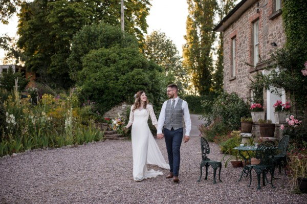 Bride and groom holding hands walking down pathway hand in hand outside wedding venue